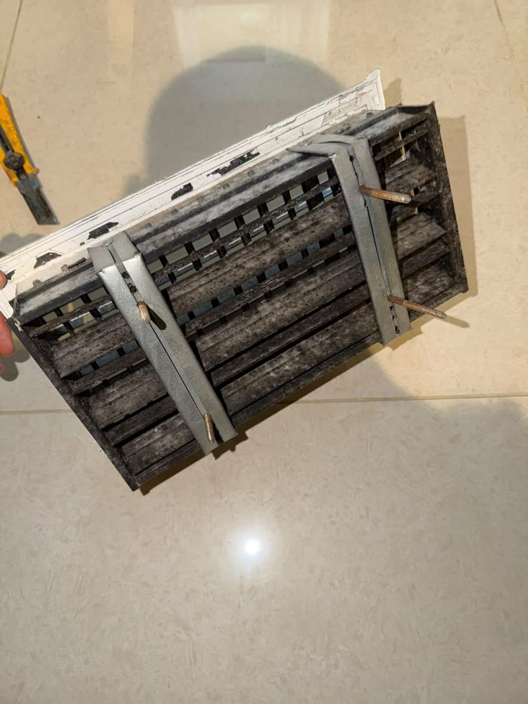 Before: an AC grille removed from the ceiling, its slats caked in dark dust